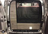 View from rear of RV rental showing wood-paneled interior, dark bed/storage area, and functional camper van setup.