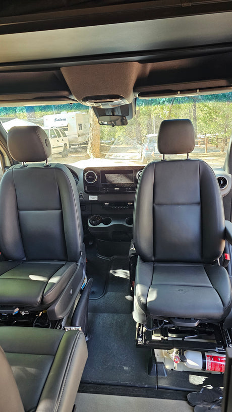Inside an RV rental: front seats, dashboard, and a view of the campground through the windshield.