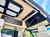 Plush RV rental interior: cream seats, dark wood overhead console, screen, and ambient lighting for luxury comfort.
