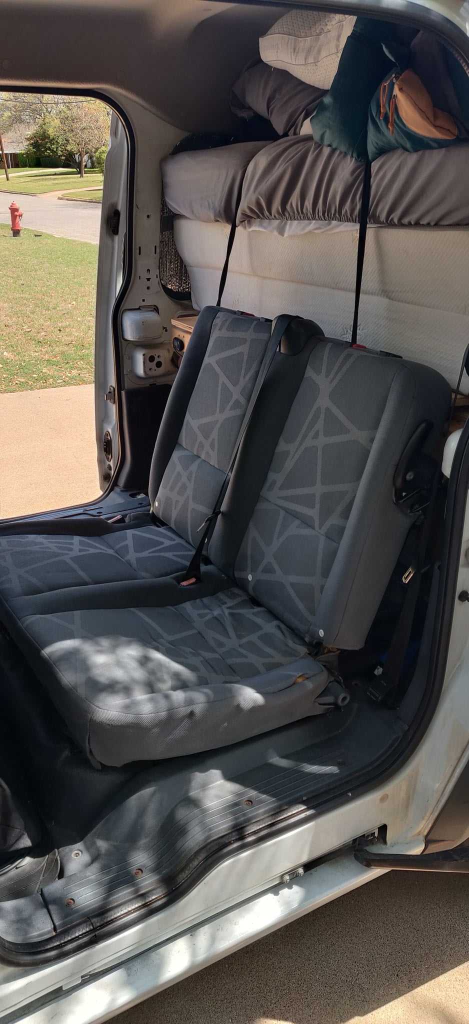 RV rental camper van interior with rear seats, an elevated bed, and an open side door facing a street. — photo 18