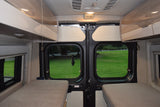 RV rental interior featuring cozy beds, overhead storage, and a scenic view through the rear doors to a grassy field.