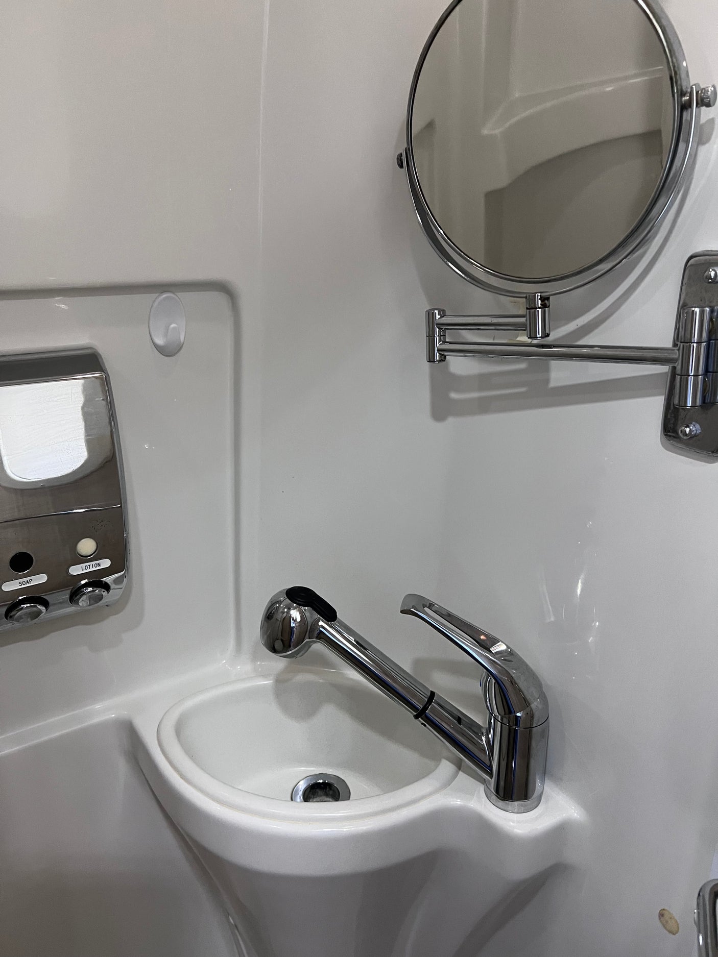 Compact RV rental bathroom with space-saving sink, pull-out faucet, soap/lotion dispenser, and wall-mounted magnifying mirror.