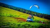 Experience adventure with a rooftop tent rv rental, paragliding over lush green hills. Perfect for scenic outdoor camping.