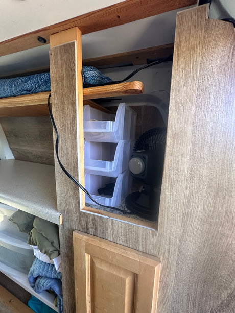 RV rental interior with built-in shelving, plastic storage bins, a fan, and a power cable for organized travel.