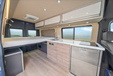 RV rental interior: cozy bed, full kitchen with Dometic fridge, and ocean views. Your compact mobile home awaits!