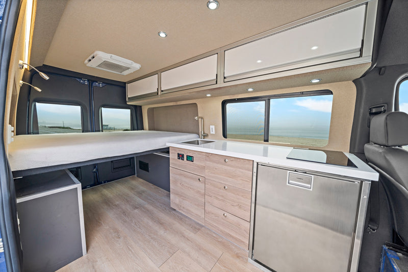RV rental interior: cozy bed, full kitchen with Dometic fridge, and ocean views. Your compact mobile home awaits! — photo 2