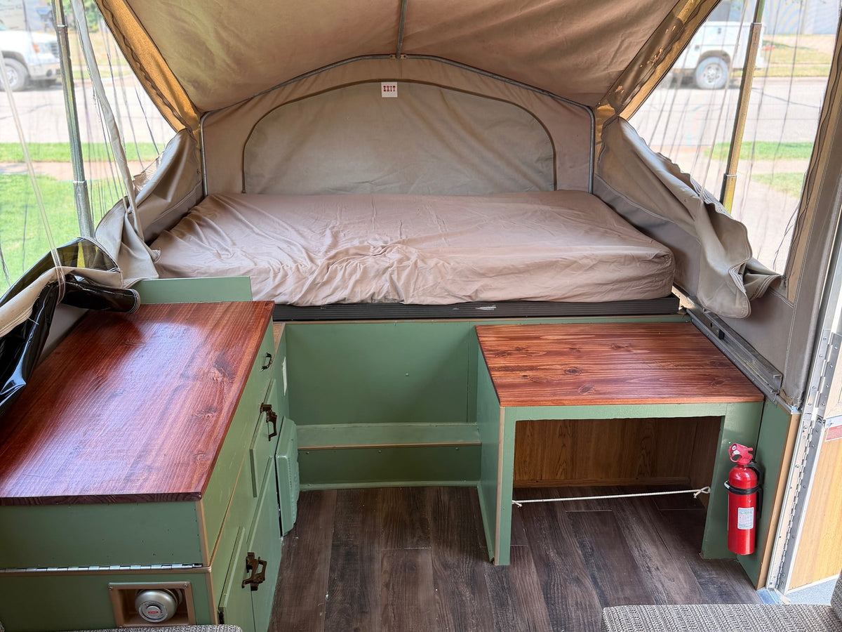  is set up for comfortable camping amidst trees under a blue sky.|Family camping fun with an RV rental pop-up camper — photo 3