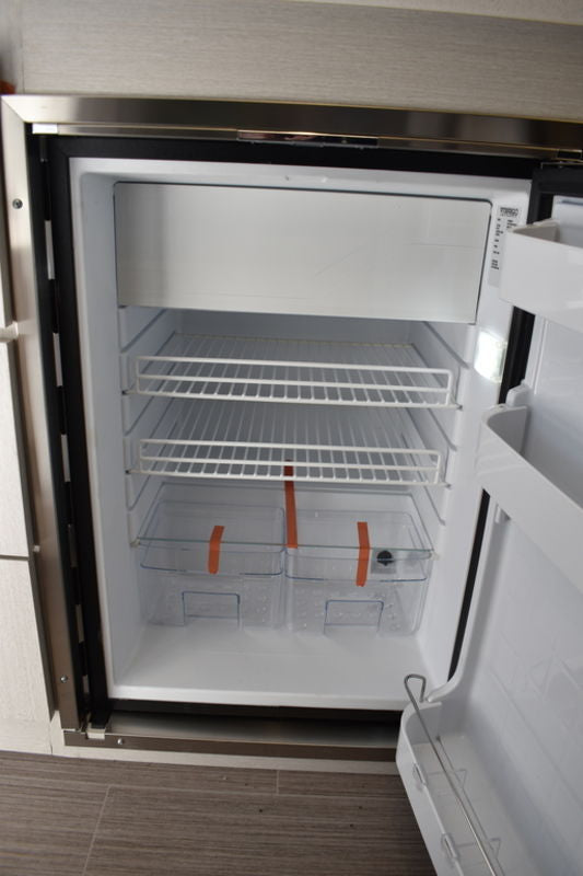 Inside an RV rental compact refrigerator: wire shelves, top freezer, and crisper bins, spotless and ready.