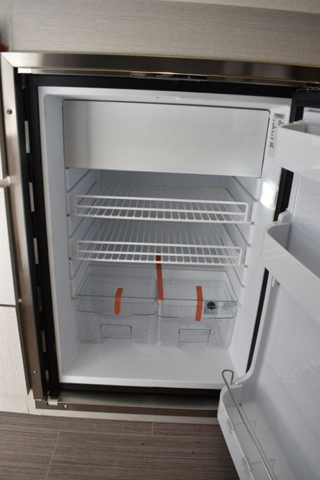 Inside an RV rental compact refrigerator: wire shelves, top freezer, and crisper bins, spotless and ready.