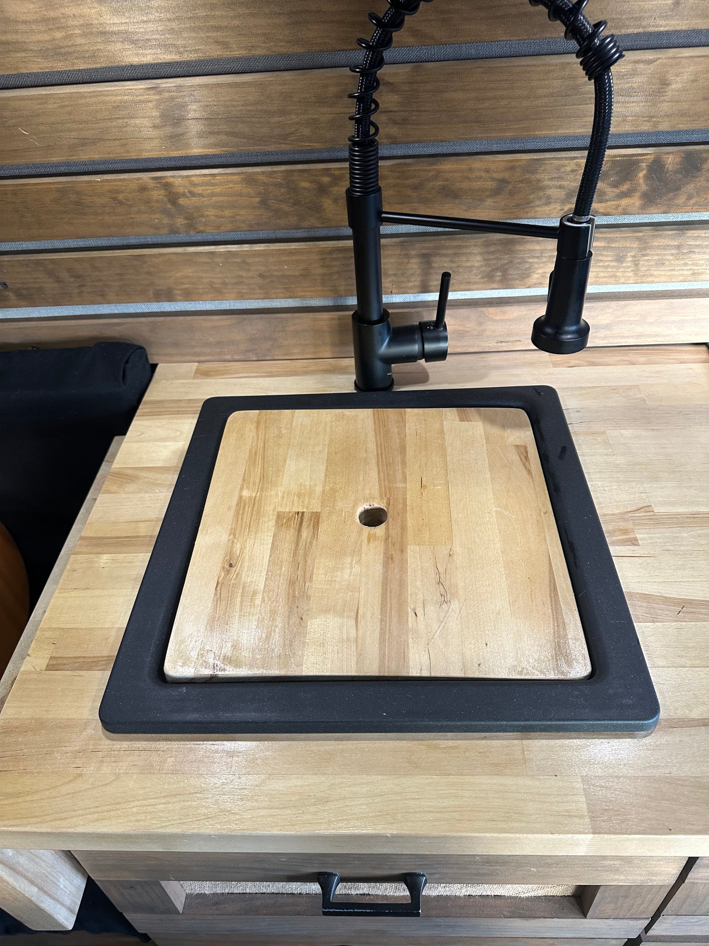 RV rental kitchen: modern black faucet, sink with wood cutting board cover, and wood countertops.