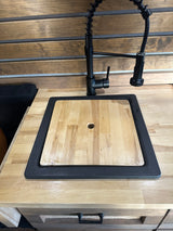RV rental kitchen: modern black faucet, sink with wood cutting board cover, and wood countertops.