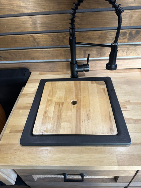 RV rental kitchen: modern black faucet, sink with wood cutting board cover, and wood countertops.