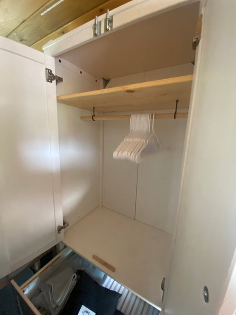 Compact RV rental wardrobe with shelf, hanging rod, hangers, and a pull-out drawer for organized storage.