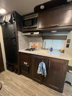 RV rental interior featuring a compact kitchen with microwave, fridge, sink, and stovetop, plus a dinette.