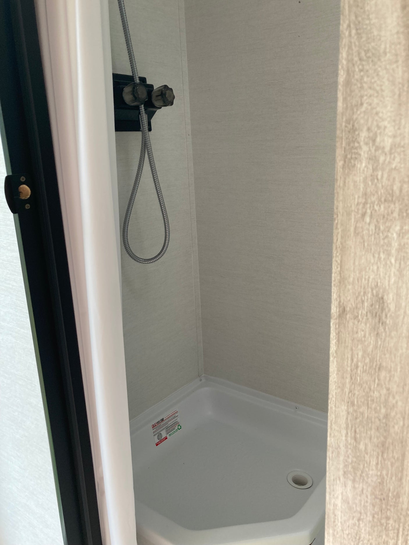 RV rental: Compact camper shower with a flexible hose and white basin, a functional space for travelers.