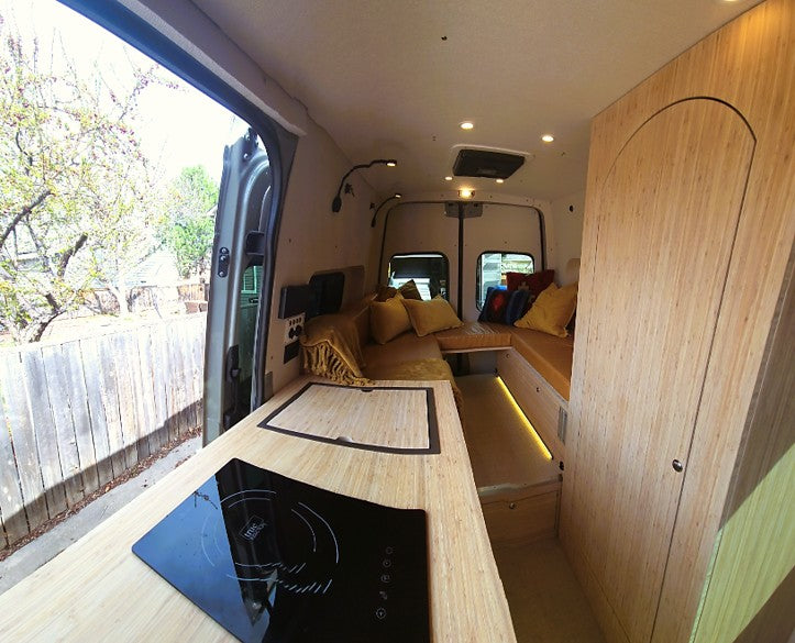 Modern camper van interior with wooden finishes, kitchen cooktop & comfy seating. Ideal for RV rental trips.