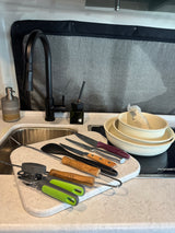 RV rental kitchen: black faucet, sink, cutting board with knives, spatula, can opener, tongs, bowls, and cooktop.
