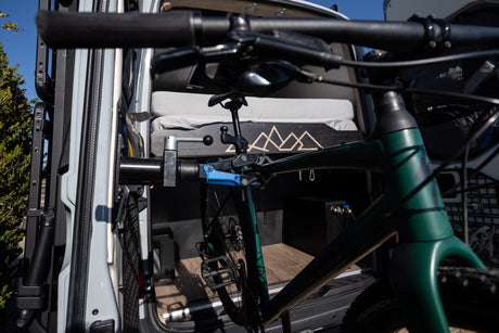 Green mountain bike neatly stored in a custom RV rental interior, featuring a cozy bed and utility storage.
