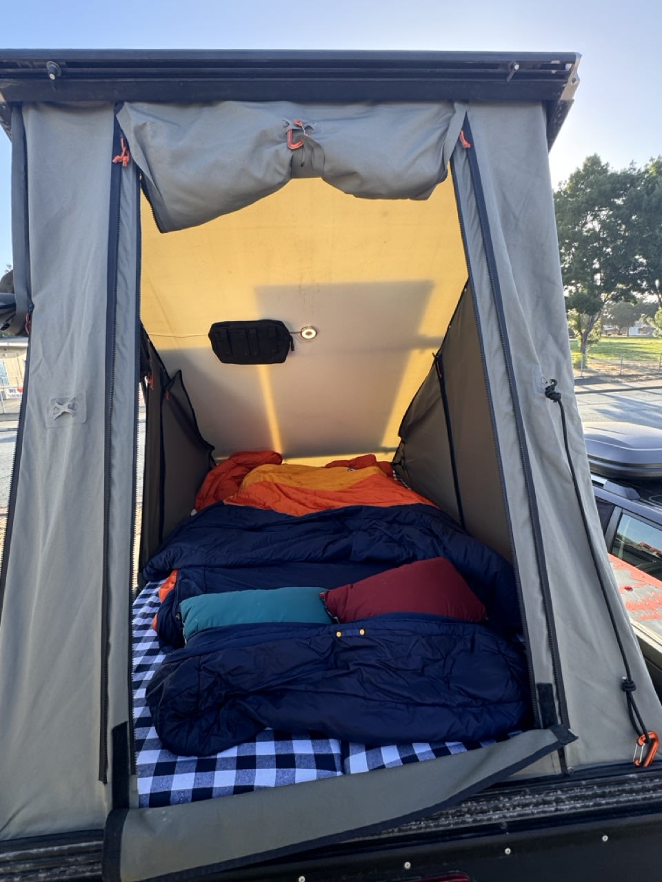Rooftop tent setup for an RV rental: a cozy interior with plaid bedding, sleeping bags, and an internal light.
