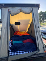 Rooftop tent setup for an RV rental: a cozy interior with plaid bedding, sleeping bags, and an internal light.