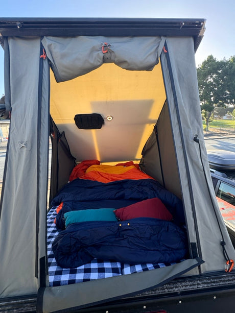 Rooftop tent setup for an RV rental: a cozy interior with plaid bedding, sleeping bags, and an internal light.