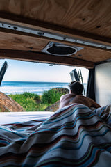 Morning calm: a person enjoys rolling ocean waves from their RV rental bed inside a camper van.