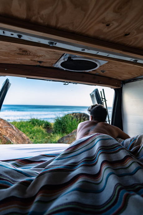Morning calm: a person enjoys rolling ocean waves from their RV rental bed inside a camper van.
