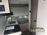 RV rental interior: compact kitchen (sink, stove), bed with plastic covering, and a wooden door. Perfect for travel.