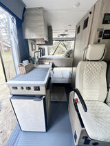 Spacious RV rental interior with modern kitchen, comfortable bed, and scenic outdoor views. Ideal for mobile travel adventures.