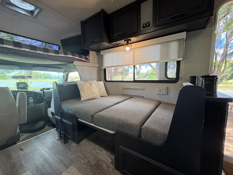 Interior of an RV rental: a modern living space with a sofa bed, bunk, and large windows revealing a scenic lake view. — photo 16
