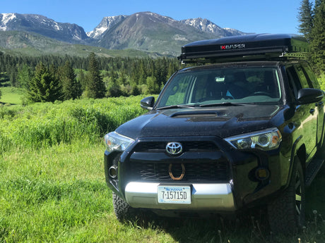 Black 4Runner with rooftop tent parked in a green mountain landscape. Explore nature; a rugged RV rental alternative for adventure.