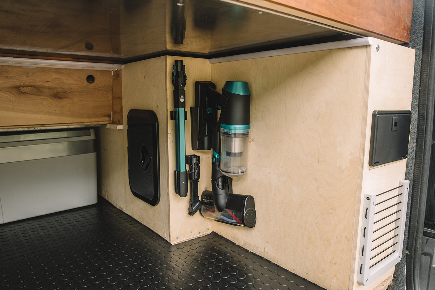 RV rental van interior features a wall-mounted cordless vacuum, attachments, and access panels for efficient, organized storage.