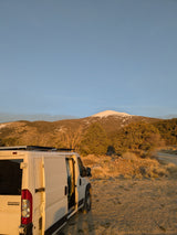 White camper van (RV rental) parked at golden hour, revealing its interior, with snow-capped mountains in the background.