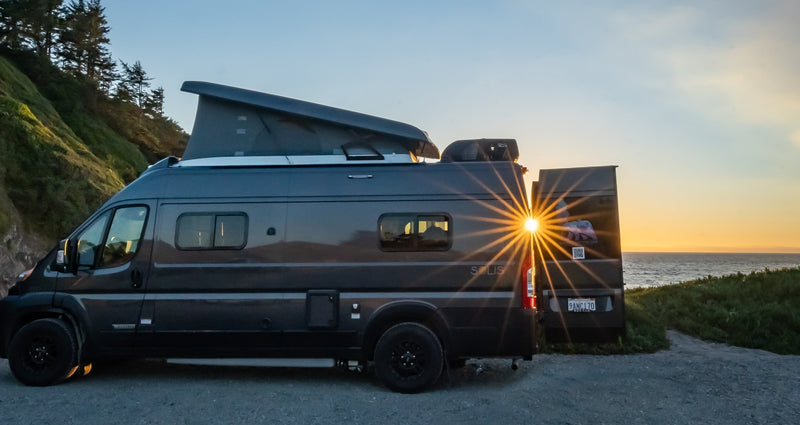 A dark grey RV rental with its pop-top extended, parked on a coastal bluff, enjoying a vibrant sunset over the ocean. — photo 1