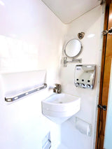 See this RV rental's compact, all-white bathroom with corner sink, mirror, dispenser, and towel bar, maximizing small spaces.