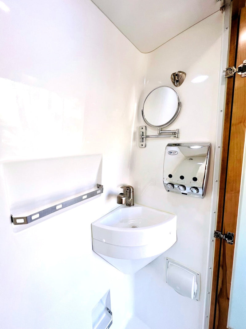 See this RV rental's compact, all-white bathroom with corner sink, mirror, dispenser, and towel bar, maximizing small spaces. — photo 17