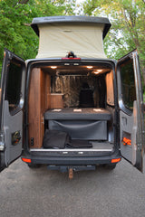Experience this custom van RV rental! Rear view reveals open doors, pop-top roof, bed, and warm wood interior.