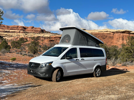 A white Mercedes camper van with a pop-top tent, an ideal RV rental for exploring scenic red rock deserts.