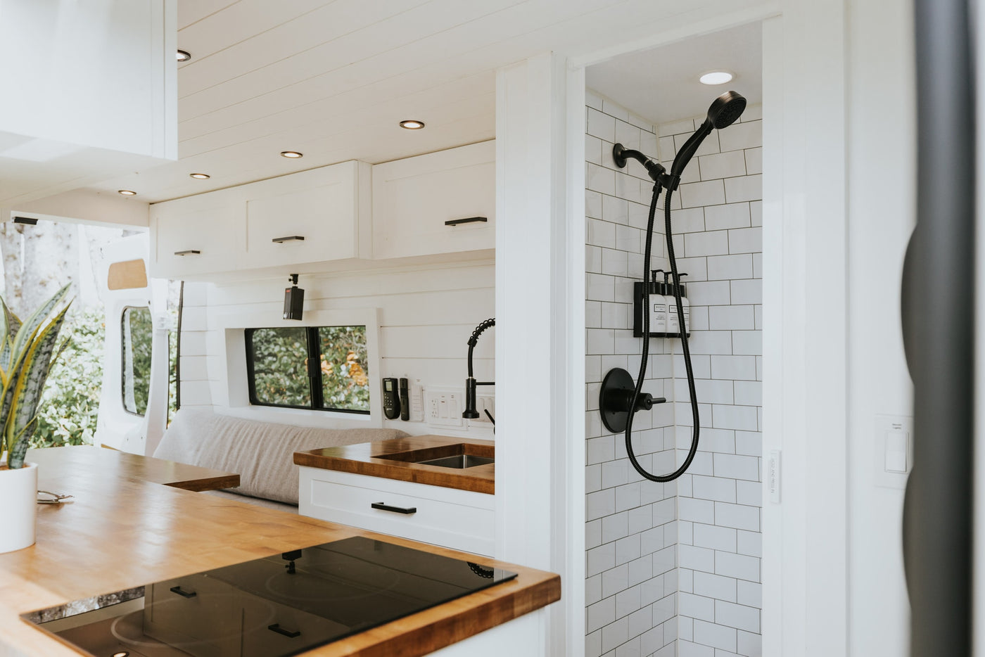Stylish RV rental interior with a compact kitchen, bed, and tiled shower in a modern van conversion. — photo 12