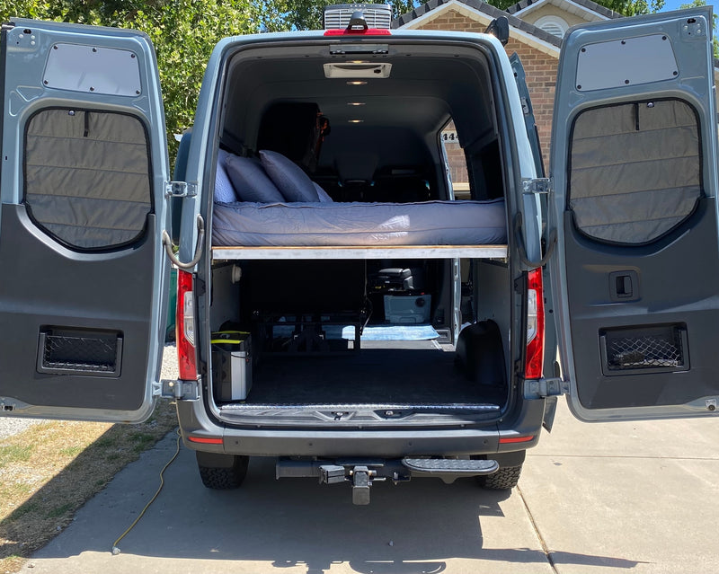 Grey camper van interior for RV rental, showing an elevated bed, under-bed storage, and open rear doors. — photo 19