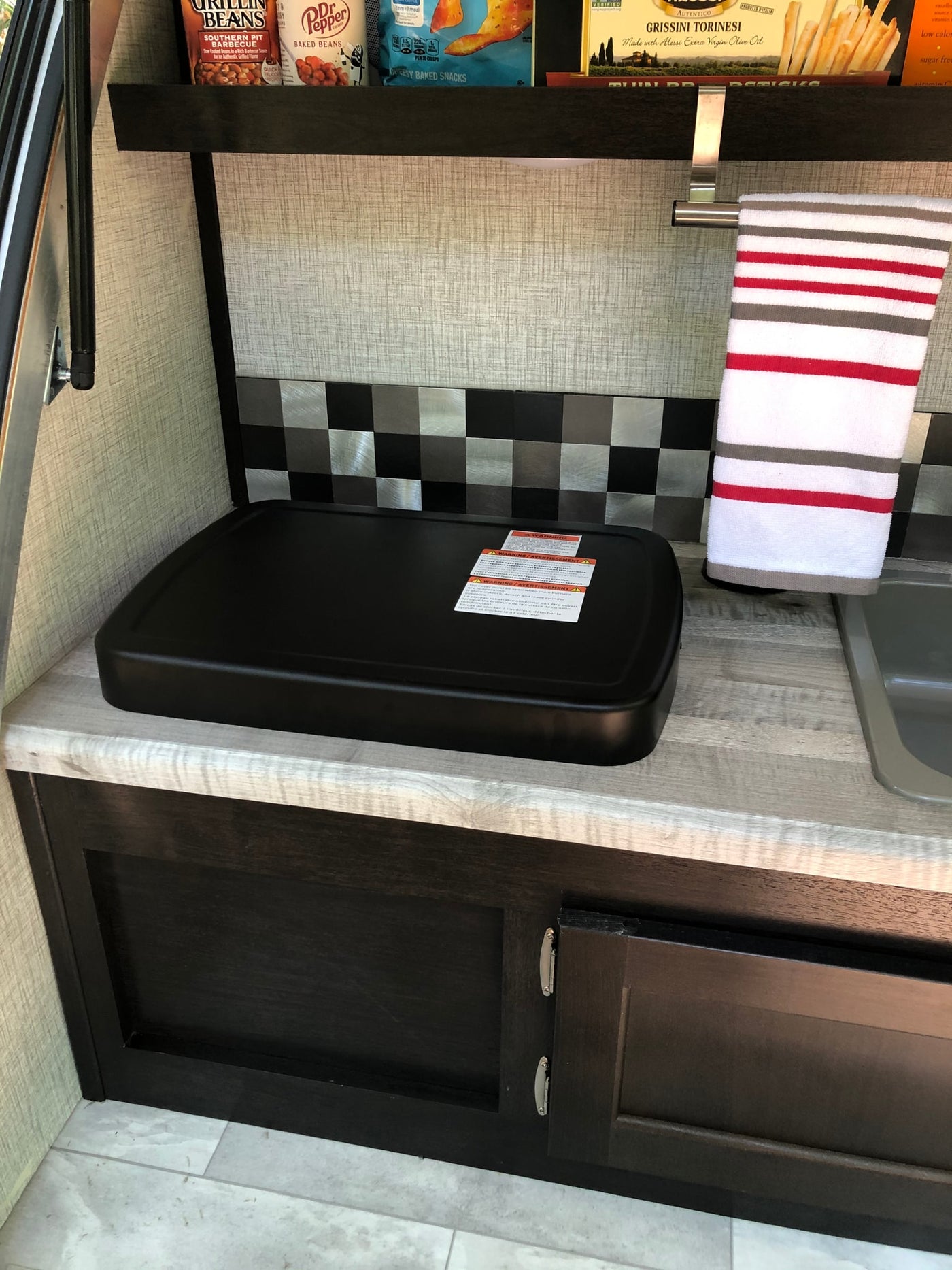 An RV rental's efficient kitchenette: griddle, sink, and a stocked shelf for travel cooking. — photo 18