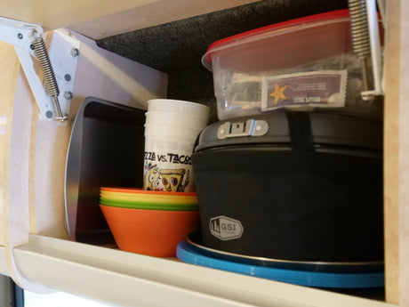 This rv rental cabinet holds kitchen essentials like stacked colorful bowls, cups, and a GSI Outdoors cooking set.