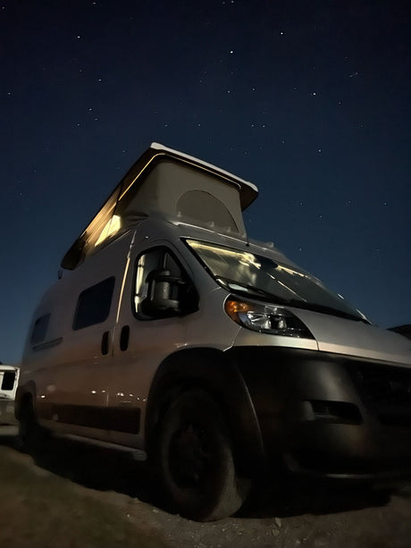 Starry night over an RV rental: a silver pop-top camper van, subtly lit. Ideal for remote camping adventures.