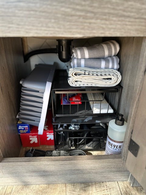 Efficient storage in an RV rental kitchen cabinet: folded towels, soap, and a collapsible dish tub.