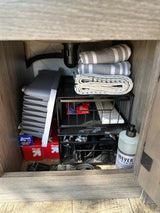 Efficient storage in an RV rental kitchen cabinet: folded towels, soap, and a collapsible dish tub.