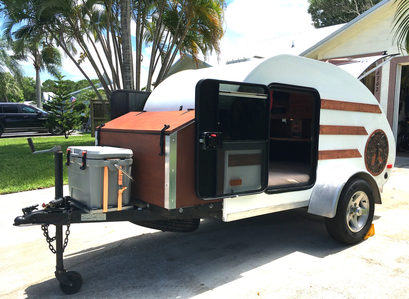 Charming teardrop camper, a perfect rv rental, with open doors revealing its cozy interior and a front cooler.