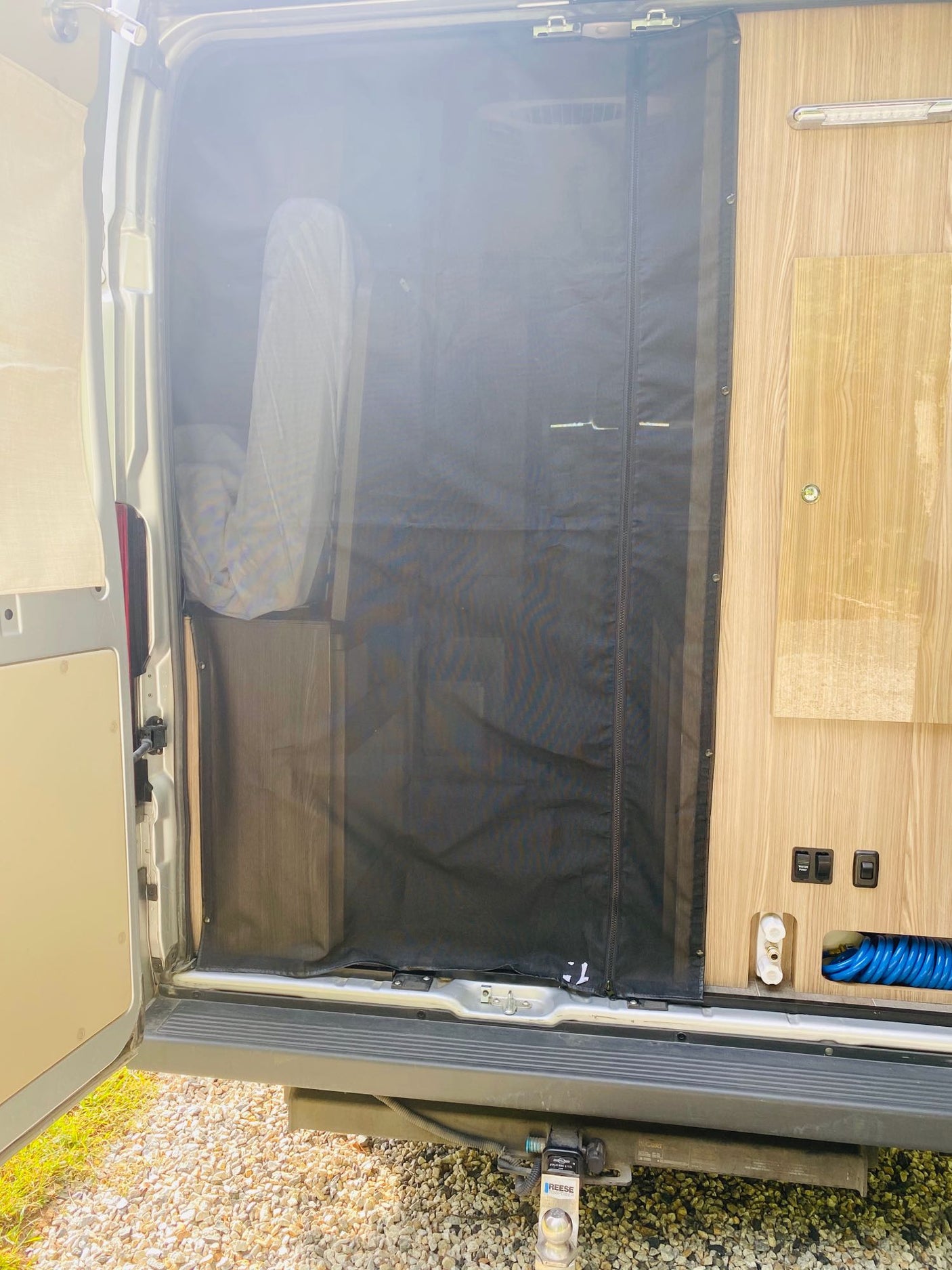 RV rental: Open rear of a van, with a black mesh screen, light wood interior, and utility features.