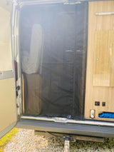 RV rental: Open rear of a van, with a black mesh screen, light wood interior, and utility features.