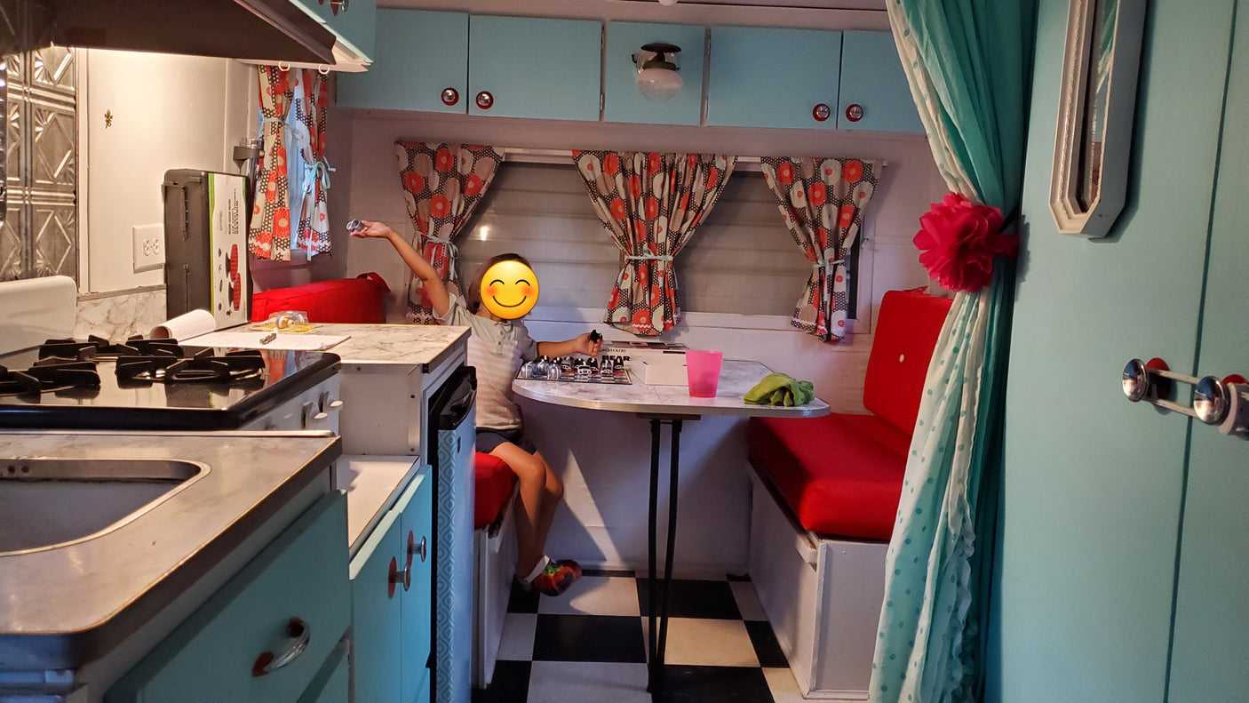 Child playing checkers inside a charming, retro rv rental, featuring a kitchen, red dinette, and checkered floor.