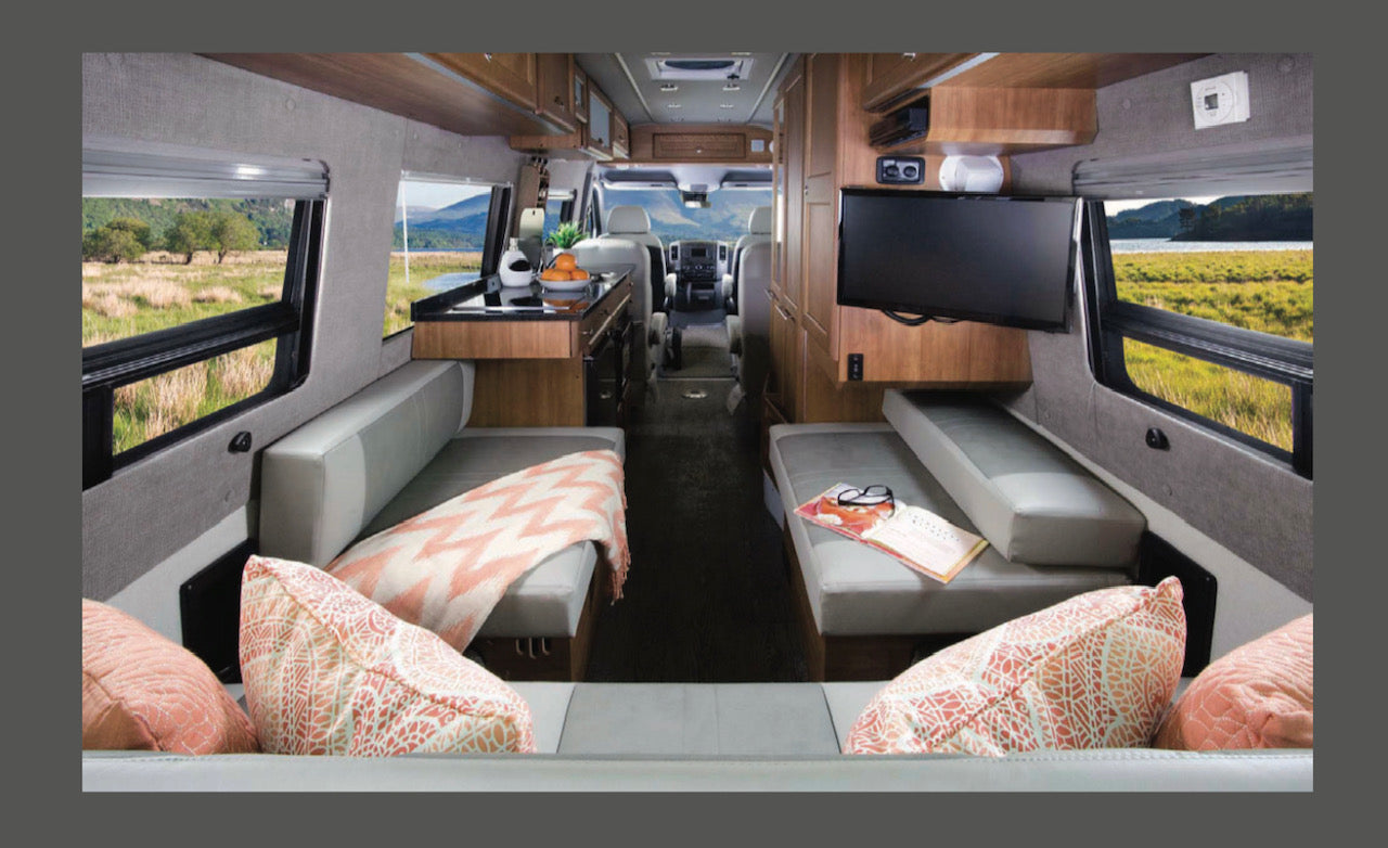 Inside a modern RV rental, featuring comfortable benches, a kitchen, TV, and large windows with beautiful outdoor views.